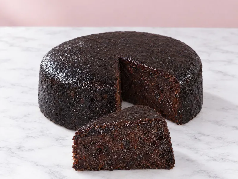 A round black cake with a wedge cut to show the dark, moist fruit crumb