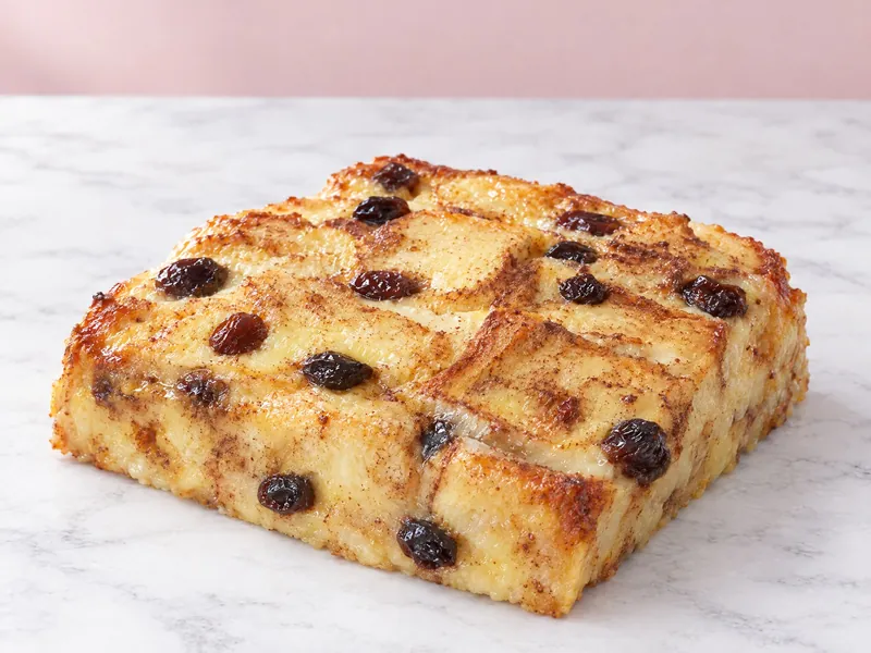 A square of bread and butter pudding, golden and dotted with raisins