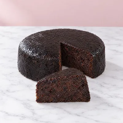 A round black cake with a wedge cut to show the dark, moist fruit crumb
